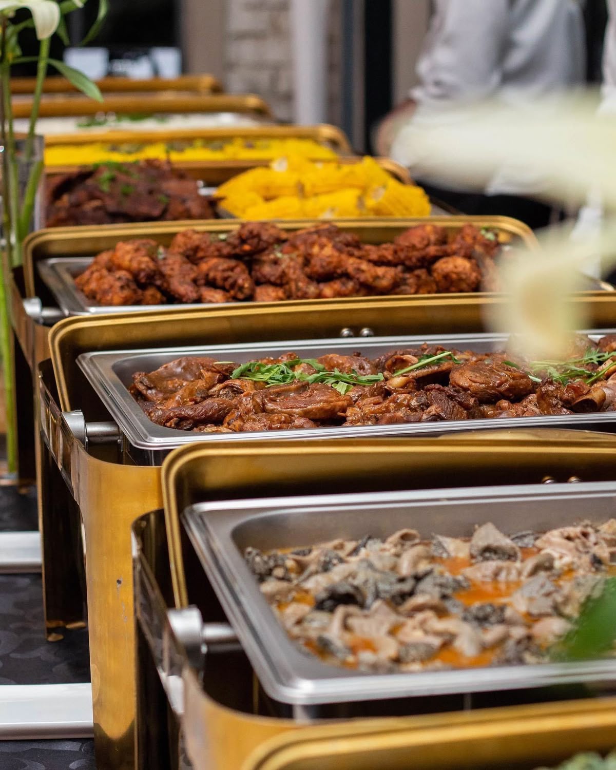 Buffet line of chafing dishes with grilled chicken wings, fish stew, and corn at a Nairobi restaurant catering event